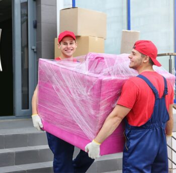 Zwei Umzugshelfer tragen ein in Folie gepacktes Möbelstück – Umzug in Bitburg