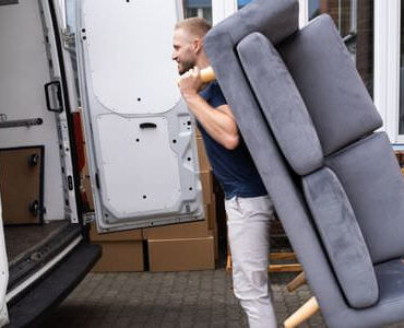 Möbellift Bitburg Möbellift Bitburg: Helfer tragen ein graues Sofa aus einem Transporter